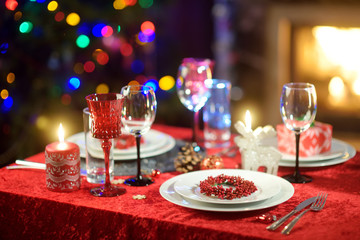 Beautiful table setting for Christmas party or New Year celebration at home. Cozy room with a fireplace and Christmas tree in a background.