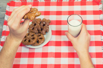 Top view om man's hands holding cookie and glass of milk over checkered table cloth