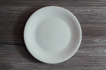 An empty white ceramic plate on grey wooden background
