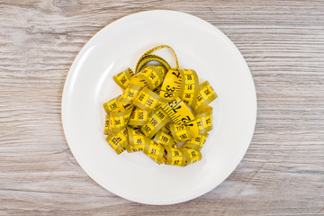 Concept of weightloss. Plate with yellow tape measure. Top view photo, wooden grey background
