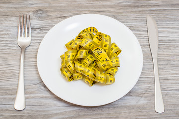 Concept of dieting. Plate with tape measure, fork and knife on wooden grey table. Top view photo.