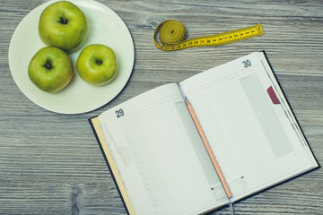 Top view on opened notebook and pencil, tlape with apples on it and tape measure on grey wooden background