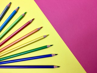 Lapices de colores formando abanico sobre fondo amarillo y rosa.