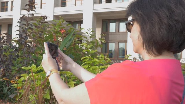 A woman in red clothes takes pictures of flowers on her mobile phone.