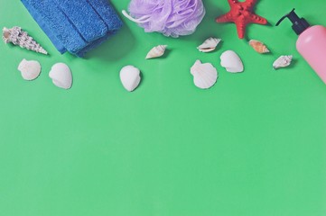 Flat lay photo bath products/ Shampoo, shower gel, blue towel and seashells on a green background