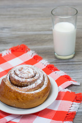 Vertical photo of appetite cinnamon roll on chechered tablecloth and glass of milk