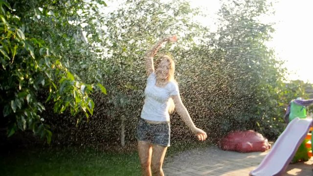 Slow motion footage of beautiful smiling young woman enjoying summer rain on sunset at backyard