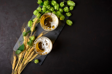 Glass of beer with green hops and wheat ears on dark wooden table. Still life. Top view