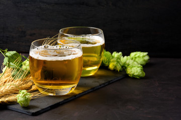 Glass of beer with green hops and wheat ears on dark wooden table. Still life