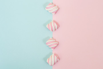 Close up photo of mini tasty marshmallows placed in line in the middle of half blue half pink background. Top view, minimal style
