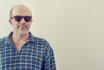 Portrait of an adult man with a gray beard with dark glasses shirt on a light background, toned.