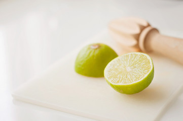 Wooden squeezer and lime cut on half on a table on a white plastic cutting board
