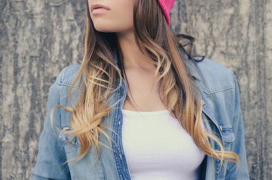 Stylish hipster woman with long hair in jeans clothing and pink hat, in white t-shirt standing against concrete wall on the street. Clopped, close-up photo, empty space on t-shirt