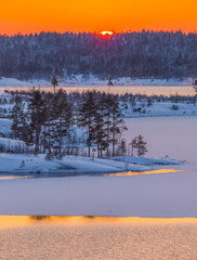 A colorful sunset on the Ladoga lake in the frost. Winter day. Open water hovers from frost. Islands in the snow.