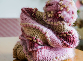 Close-up of a hand-knit winter hat in modern colors, beige, rose ash and cherry. Thick and warm woolen yarns suitable for cold winter days. Shallow depth of focus. Hobby concept.