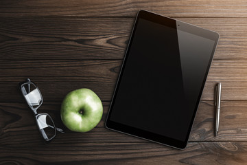 Tablet in high definition with eyeglasses, silver pen and green apple on a wood background. Top view