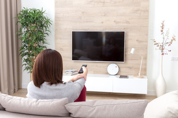 Young woman watching TV in the room sitting on a couch with remote control