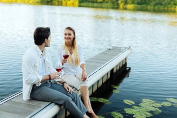 Romantic place. Delighted joyful couple sitting near the river while enjoying their wine