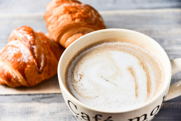 large beige Cup of coffee with milk and croissants on a wooden table. on the Cup inscription in French (top down: mocha coffee, coffee with milk, coffee without sugar)