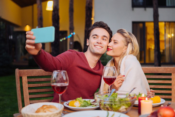 Our photo. Joyful nice man smiling while taking a selfie with his girlfriend in the restaurant