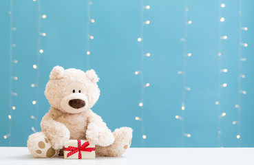 A teddy bear and gift box on a shiny light blue background