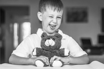 Funny and naughty Caucasian child with a toy teddy bear. Kid showing tongue. Happy childhood...