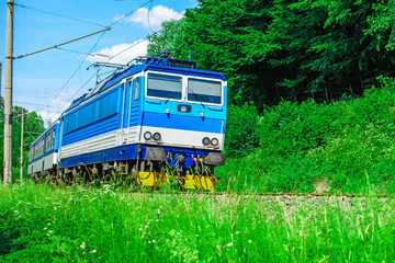 A blue electric locomotive passing the Czech countryside. A train running through the green valley....