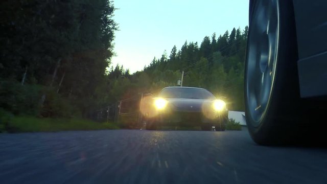 Low-angle shot of a Ferrari following behind a Lamborghini down a winding country road at dusk.