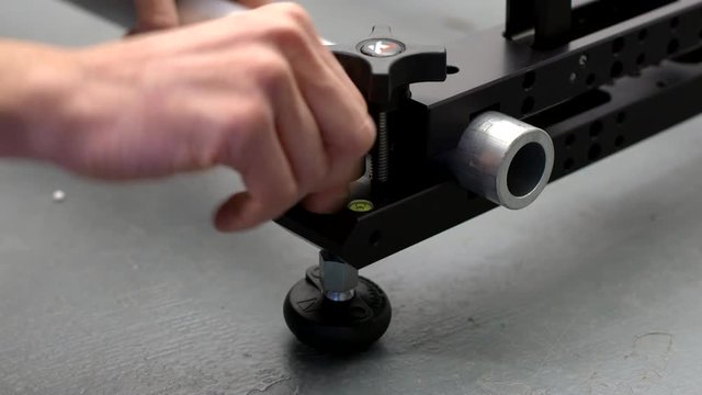 Male hand adjusting a levelling foot on a a camera dolly slider clamp holding speed rail.