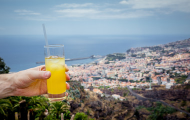 Drinking orange cocktail of Poncha on Madeira island, man holding a glass with drink, blurred city...