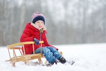 Funny little girl having fun with a sleigh in beautiful winter park. Cute child playing in a snow.