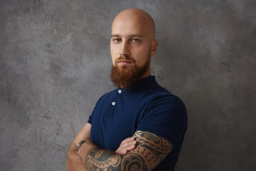 Isolated shot of fashionable stylish serious young male with shaved head, tattoo fuzzy ginger beard...
