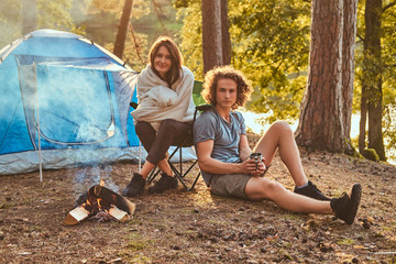 Couple hiking at in the forest. Attractive couple warming near a campfire at camp.