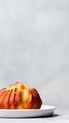 Close up of large delicious profiteroles with custard served on a white plate on a gray background.