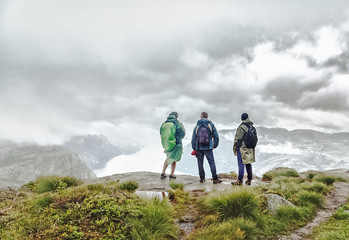 Three male person looking away standing at the edge of cliff over canyon in Norway. Hiking concept. Great Northern nature of Norway and Scandinavia. Preikestolen famous and popular landmark in Norway.