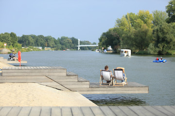 Para młodych ludzi odpoczywa na leżakach nad rzeką Odrą we Wrocławiu. - obrazy, fototapety, plakaty