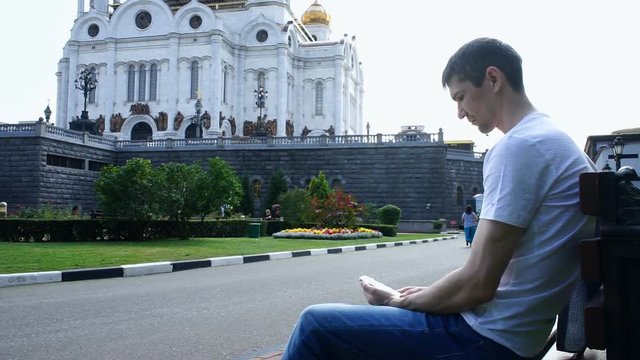Man is sitting with a phone near the church