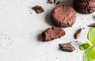 Chocolate cookies with pieces of chocolate and mint on a grey concrete background. Selective focus.