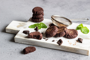 Chocolate cookies, pieces of chocolate, mint and cocoa powder on a white wooden cutting board. 