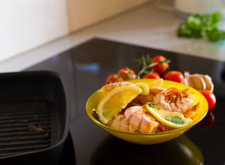 Food. Langoustines, induction stove, yellow plate, grill pan, tomatoes, lemon