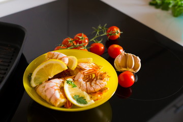 Food. Langoustines, induction stove, yellow plate, grill pan, tomatoes, lemon