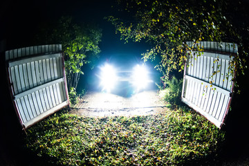The car stands on the territory of the house at night. Light headlights through the fence