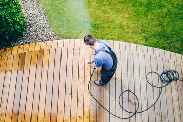 man cleaning terrace with a power washer - high water pressure cleaner on wooden terrace surface - 222211551