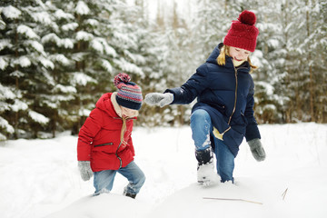 Two adorable little girls having fun together in beautiful winter forest. Beautiful sisters playing in a snow.