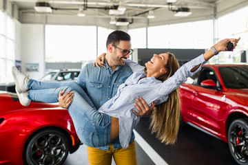 Beautiful young couple at car showroom exited because of buying a new car.