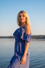 Young woman in a beautiful dress is standing on the river bank, free space.