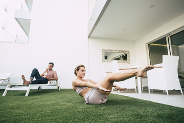 nice blonde young girl doing pilates at home in the garden while the handsome boyfriend stay...
