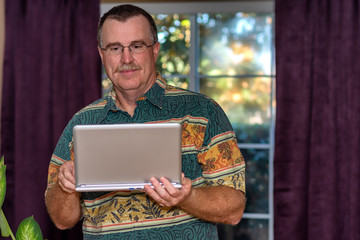 Senior male standing using a laptop computer at home