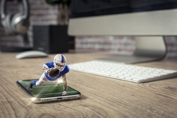 Football Player with a blue uniform playing and coming out of a full screen phone on a wooden table.