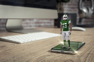 Football Player with a green uniform playing and coming out of a full screen phone on a wooden table.